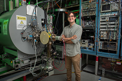 A graduate student stands near the device he uses in the Low Energy Beam and Ion Trap (LEBIT) area of the laboratory.