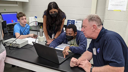 A research team of three students and an instructor gather around a laptop while working on the identification of an unknown radioactive source through gamma spectroscopy at this year’s Physics of Atomic Nuclei program.