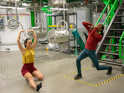 Two people dance in front of scientific equipment at FRIB.