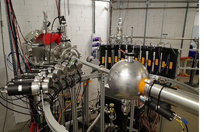 The photo shows the setup on the general-purpose beamline in the new ReA6 vault. The ODeSA detectors are on the left, and the NEXT detectors are on the right, forming a semicircle around the spherical target chamber.