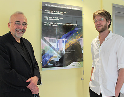 Witek Nazarewicz (FRIB Chief Scientist) and Léo Neufcourt (Research Associate) shake hands in front of an FRIB poster.