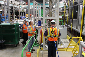 Three FRIB employees lower the vertical beamline into the front end of the facility. 