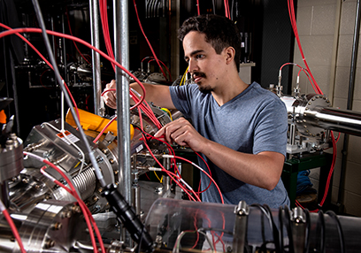 A graduate student adjusts red wires on the beamline in the Low Energy Beam and Ion Trap (LEBIT).