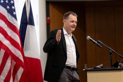 An American flag is in the foreground (left) and a French flag is behind him.