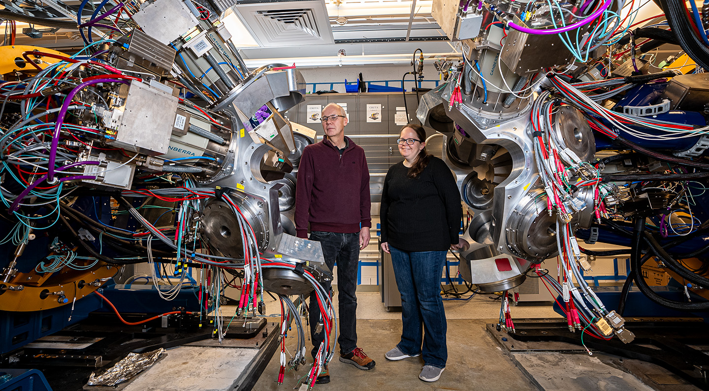 Two people surrounded by a large aluminum sphere with dozens of cables.