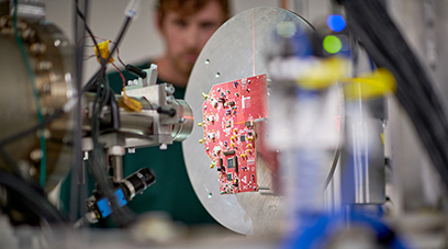 Photo of a microchip with scientific equipment. A researcher stands in the background.